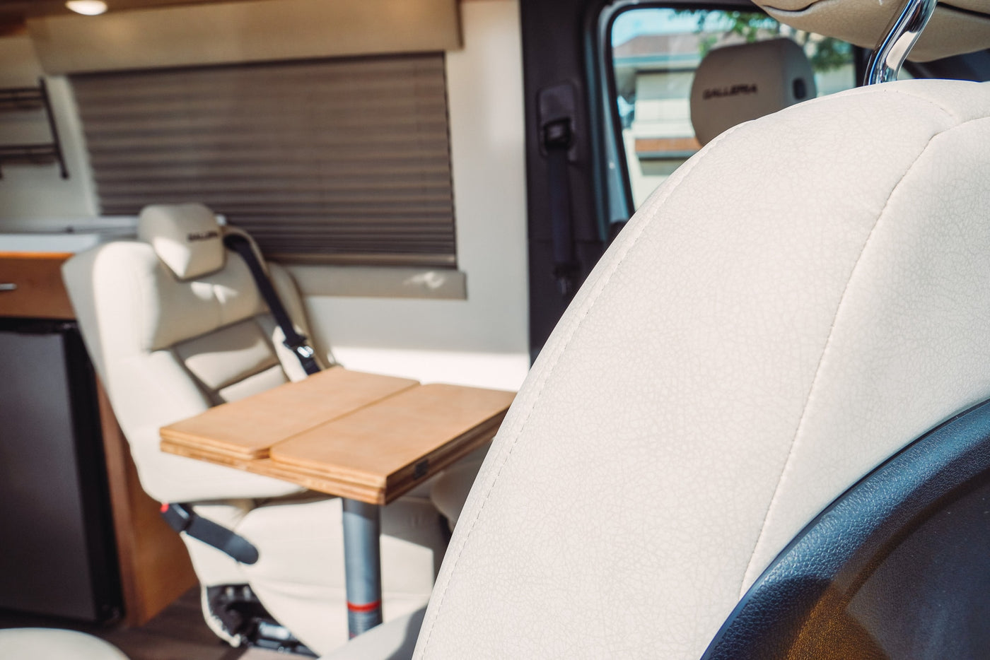 Inside a modern RV rental, showing cream seats, a wooden table, and a mini-fridge for comfortable travel. — photo 13