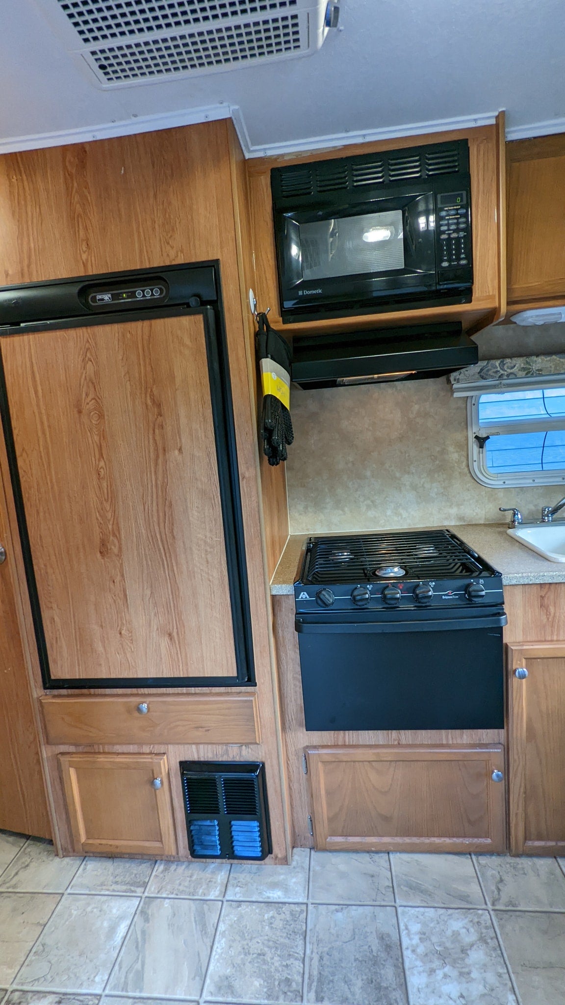RV rental kitchen: This interior view shows a wood-look refrigerator, black microwave, and stove with a sink and tiled floor.