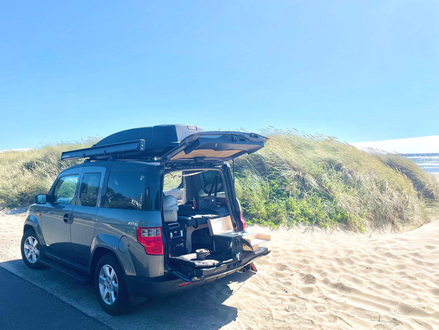 Modified Honda Element with camping gear and roof box at the beach. Ideal for a compact RV rental road trip.