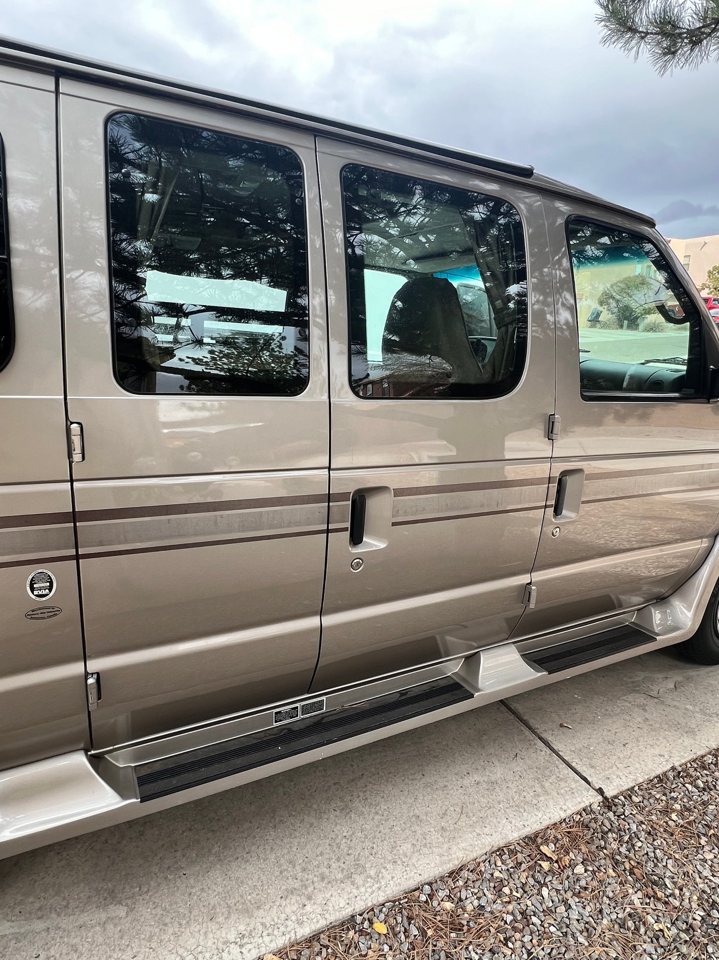 Side view of a beige RV rental van, showing its windows, passenger doors, and running boards. Ideal for road trips.