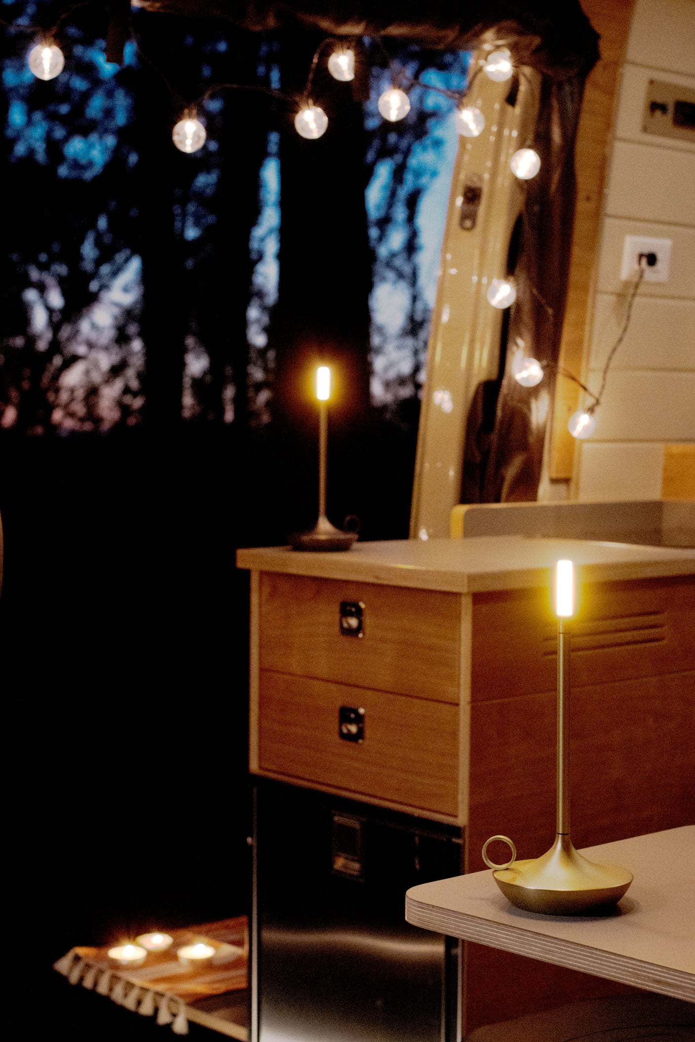 Serene RV rental interior at night, illuminated by modern lamps, string lights, and soft candles. Wood details.