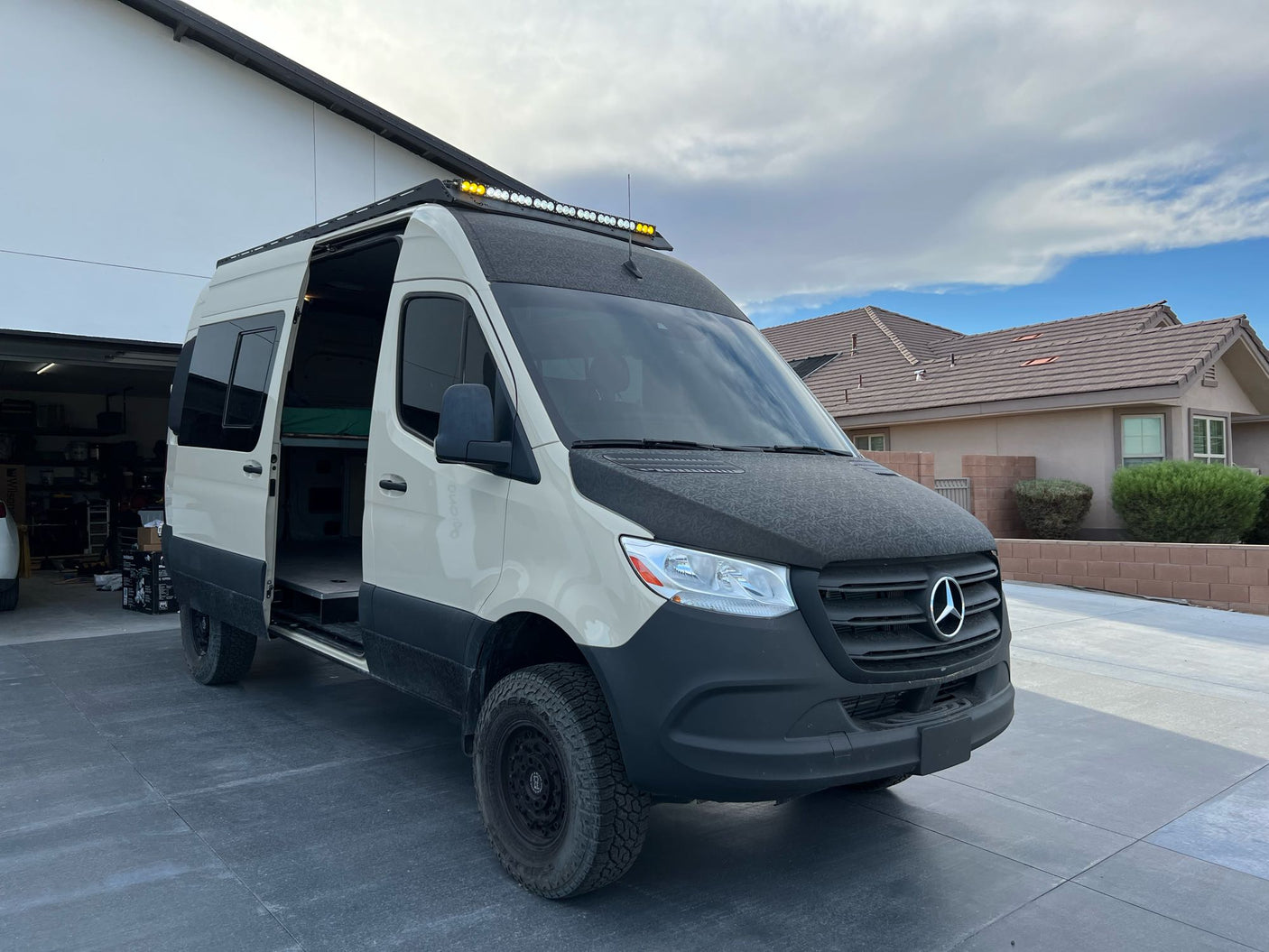 Rugged Mercedes-Benz Sprinter adventure van parked on a driveway with side door open, ideal for an rv rental.