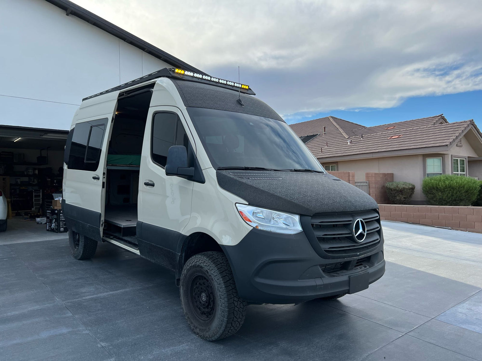 Rugged Mercedes-Benz Sprinter adventure van parked on a driveway with side door open, ideal for an rv rental.