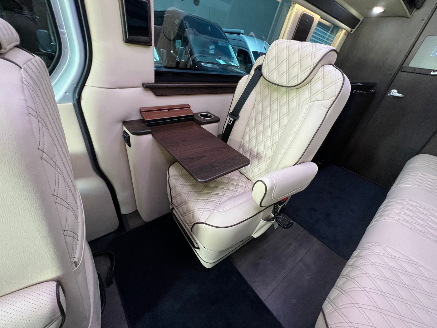 Inside a luxury RV rental: cream diamond-quilted captain's chair, dark wood table with cupholder, and comfortable rear seating. — photo 12