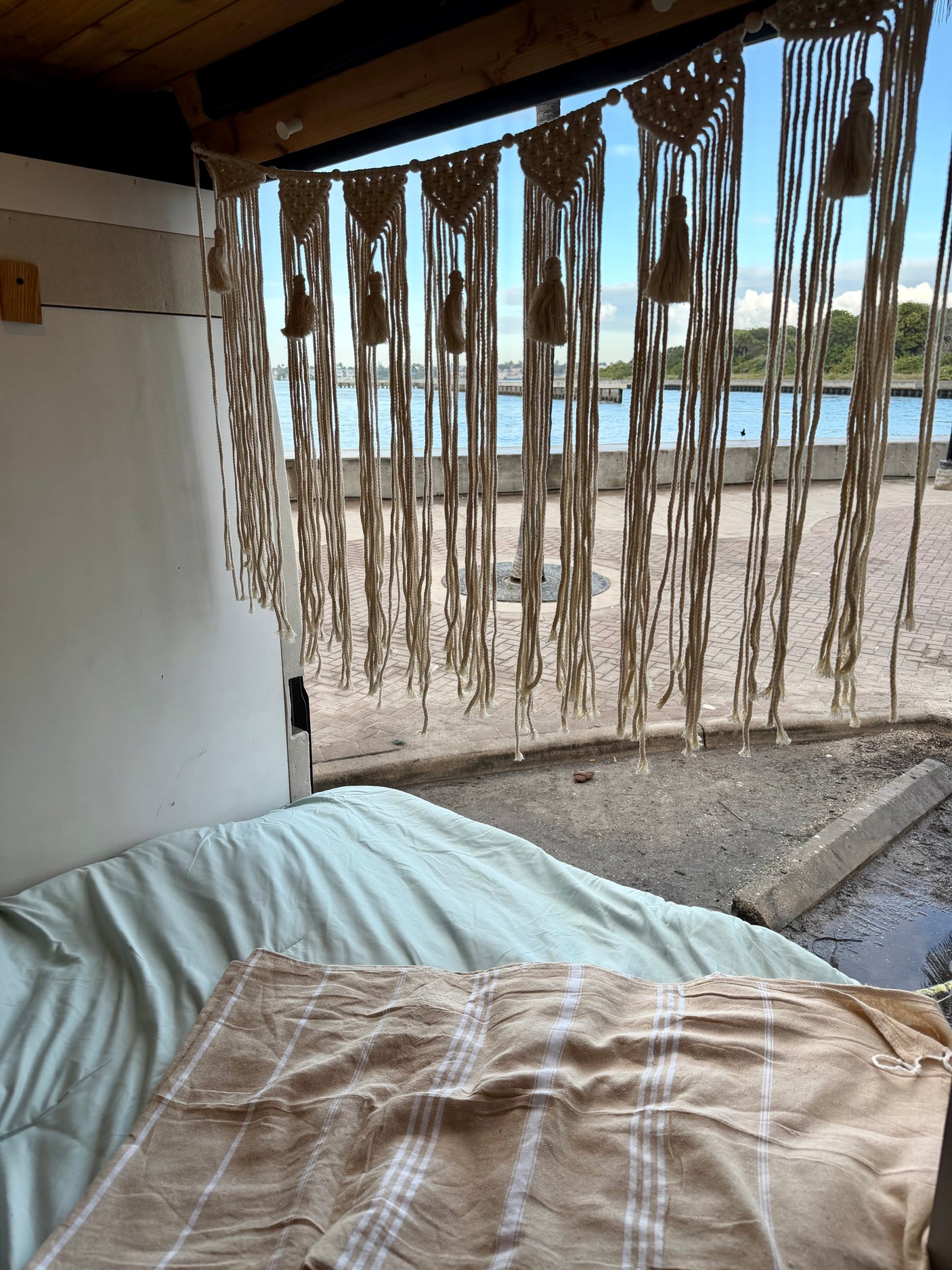 Cozy RV rental interior with a bed, macrame decor, and a scenic water view from the open back.