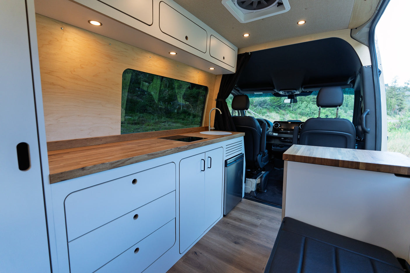 Inside an rv rental, a modern camper van kitchen with wooden counters, white cabinets, and spacious design, ready for your next road trip.