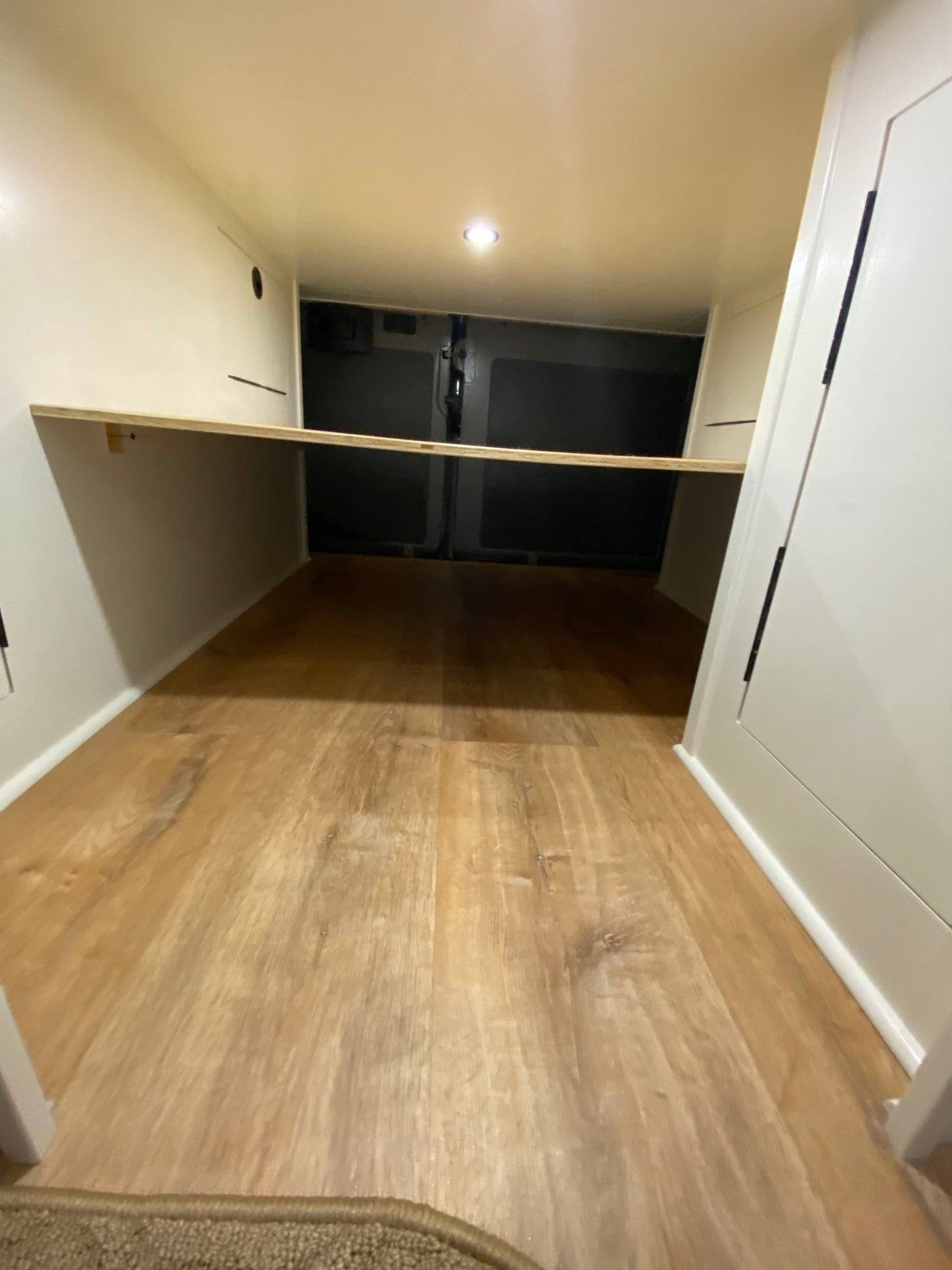 RV rental camper van interior: light wood flooring, white walls, and versatile shelf, ideal for bed or gear storage.