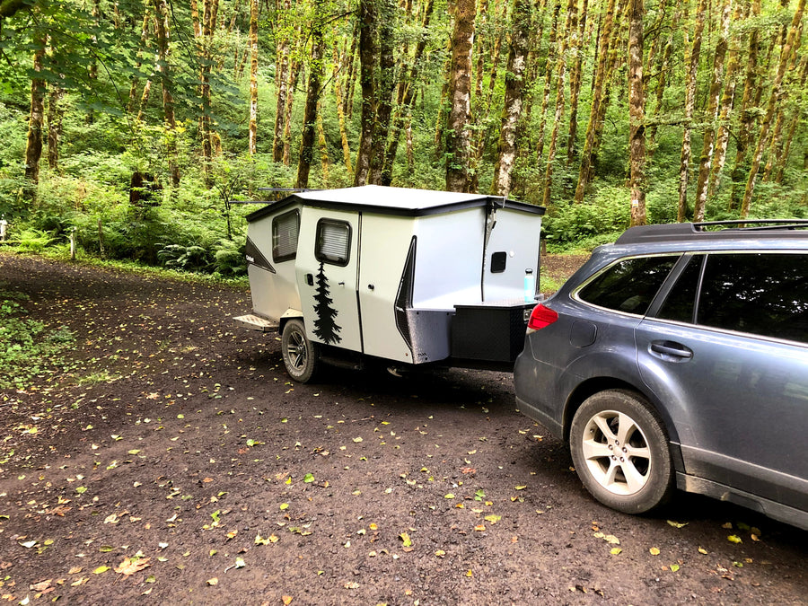 Car towing an RV rental camper in a lush, mossy forest campsite, perfect for nature getaways.