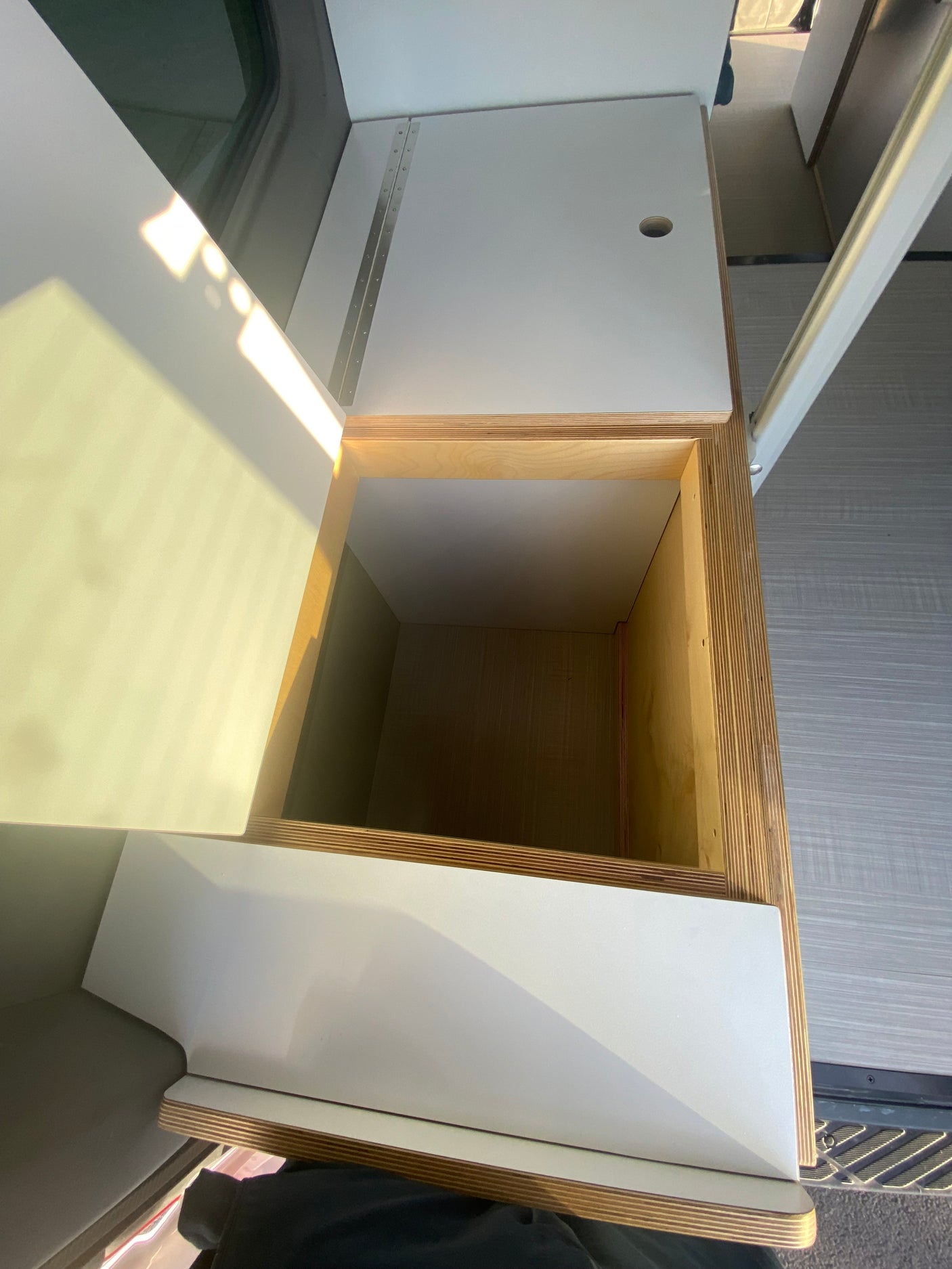 Explore this RV rental's modern interior: open top-loading storage, sleek white surfaces, and custom plywood accents.