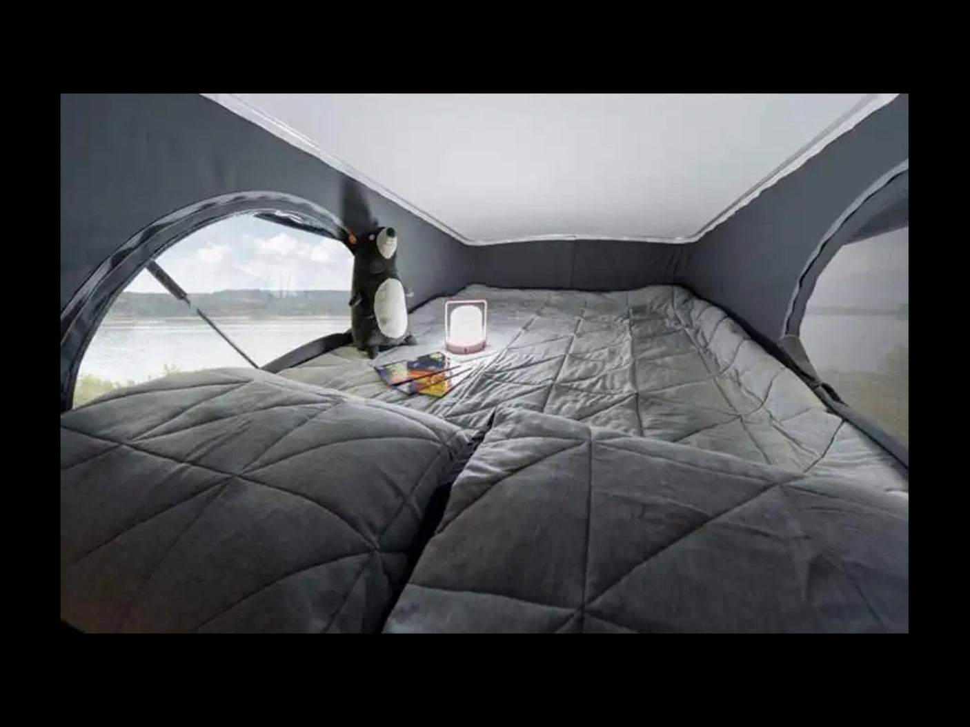 Cozy RV rental interior: quilted bed, large window with water view, plush toy, and lantern for comfy travel.