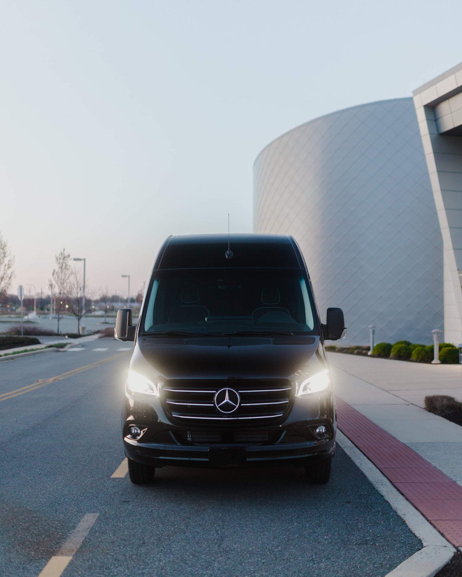 Sleek black Mercedes-Benz Sprinter van, a great RV rental option, parked with bright headlights on.