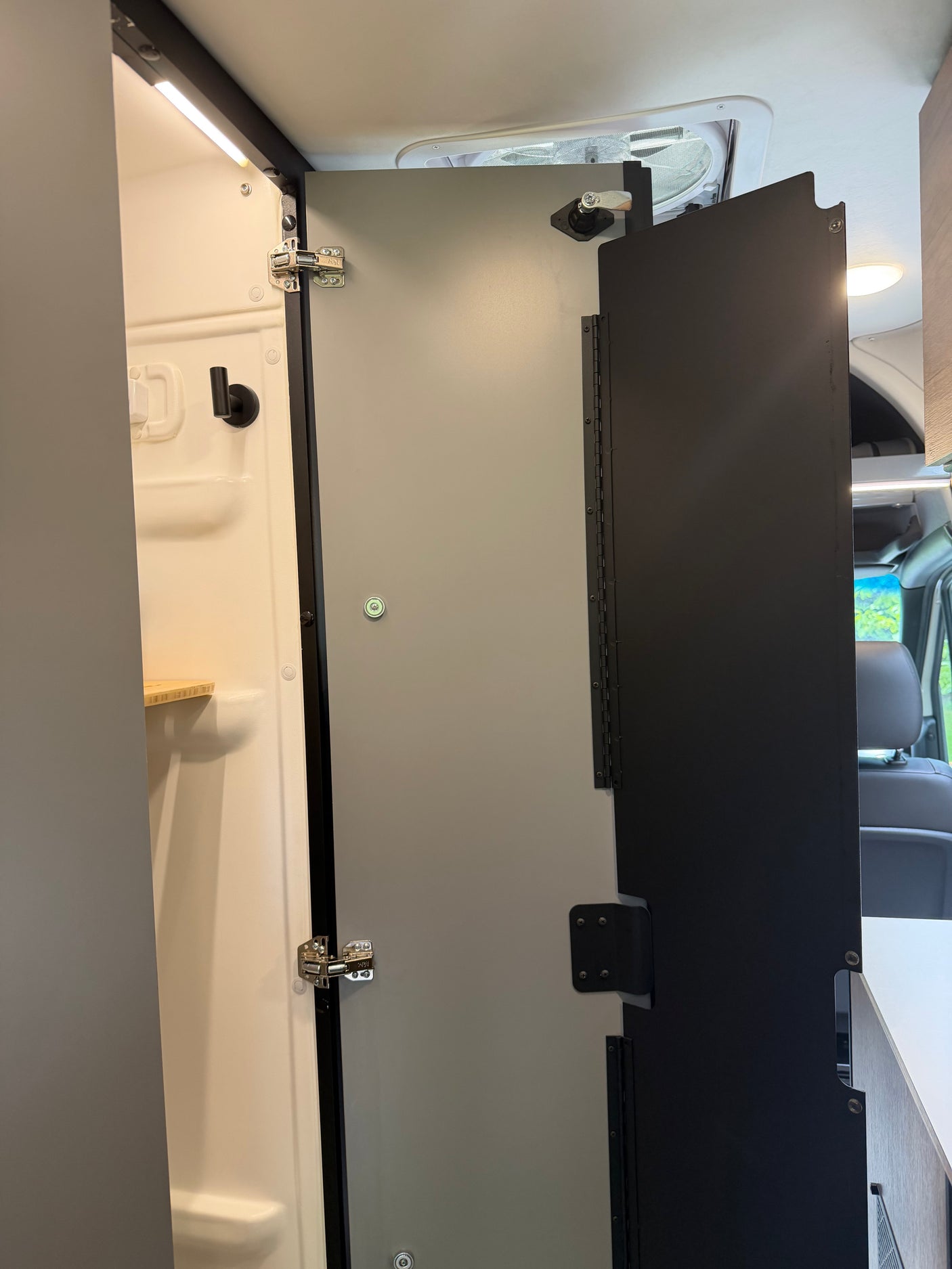 Compact RV rental camper van interior: shower stall with smart folding door system and overhead lighting.