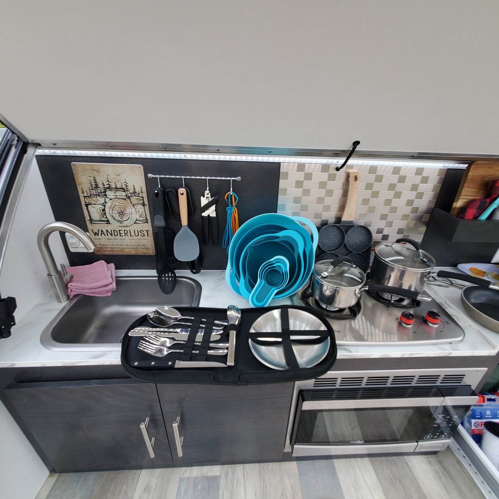 RV rental kitchen featuring a compact stainless steel sink, two-burner stove, microwave, and organized cooking tools.