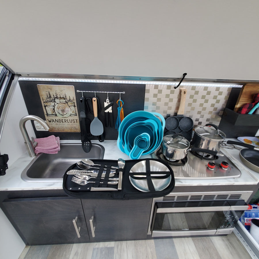 RV rental kitchen featuring a compact stainless steel sink, two-burner stove, microwave, and organized cooking tools.