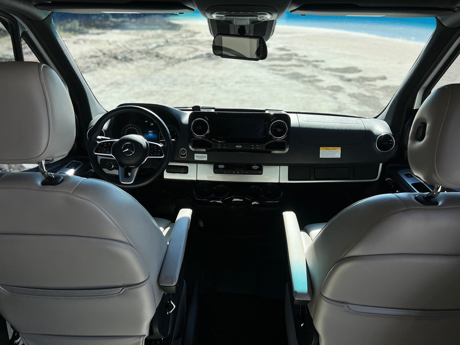 Modern RV rental interior with a Mercedes-Benz dashboard, comfortable seats, and a view of a sandy, open landscape.