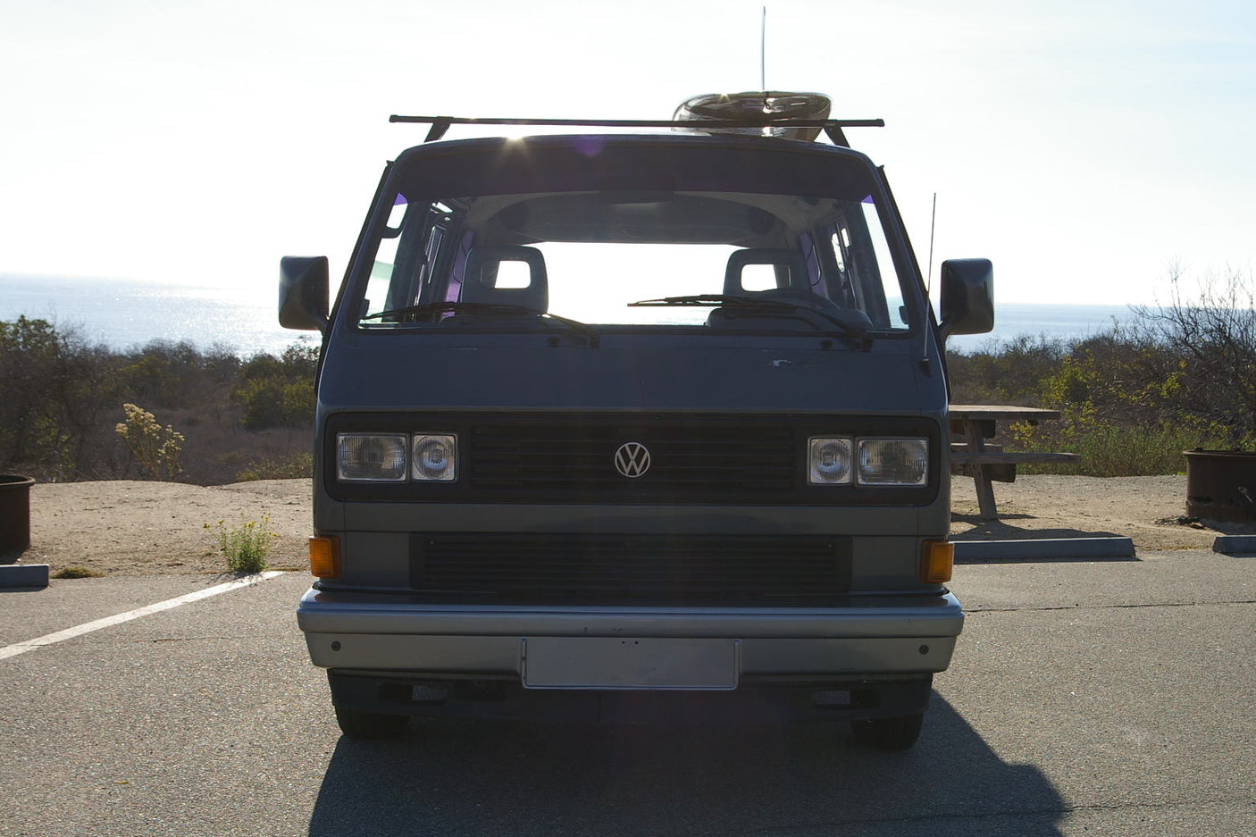 Front view of a gray VW Vanagon camper van parked at a scenic ocean-side campsite. Ideal RV rental for your next adventure.