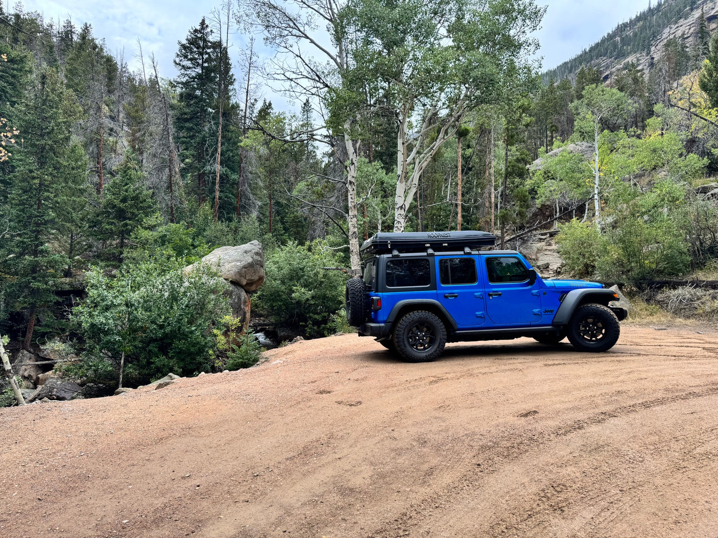 Blue Jeep with rooftop tent on a scenic dirt mountain road. This rugged vehicle is perfect for an adventure-focused rv rental.