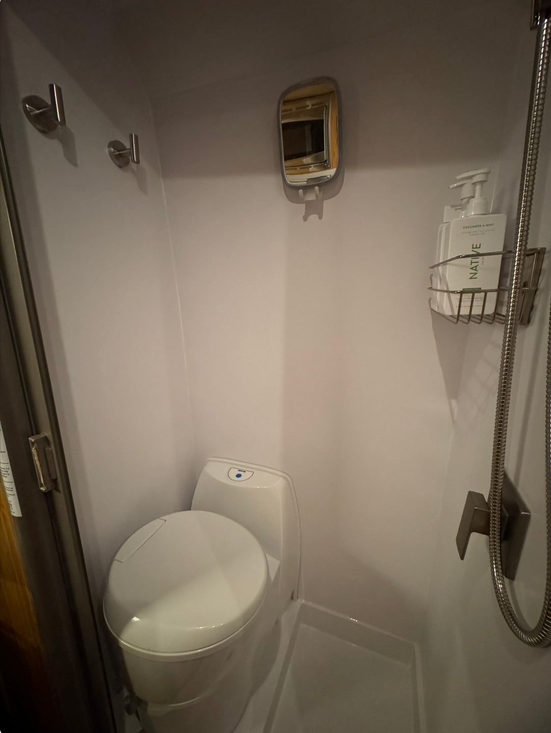 RV rental bathroom features a compact toilet, shower, mirror, and hooks. Essential amenities for travel comfort.