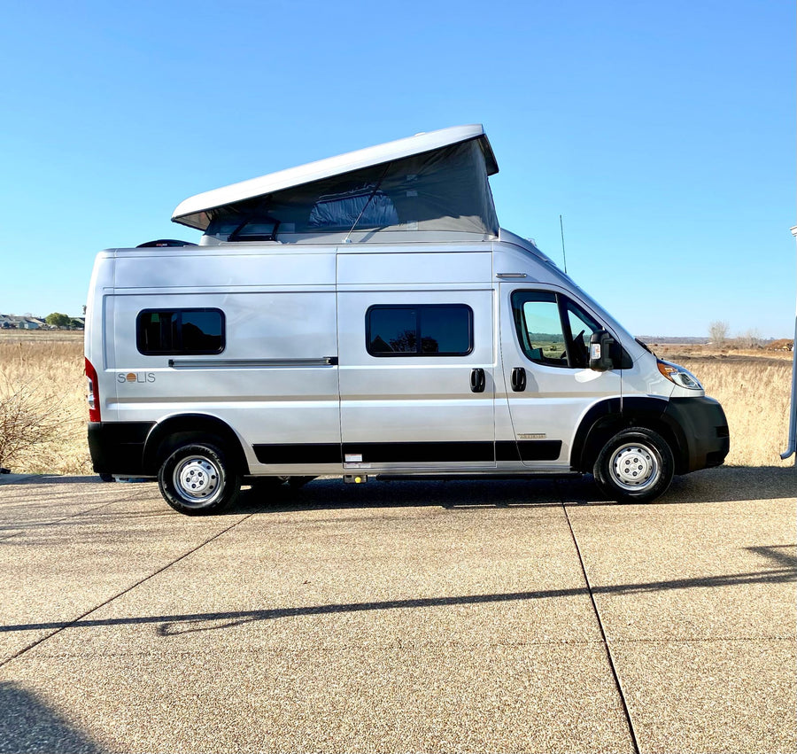 Side view of a silver Winnebago Solis camper van with its pop-top roof raised