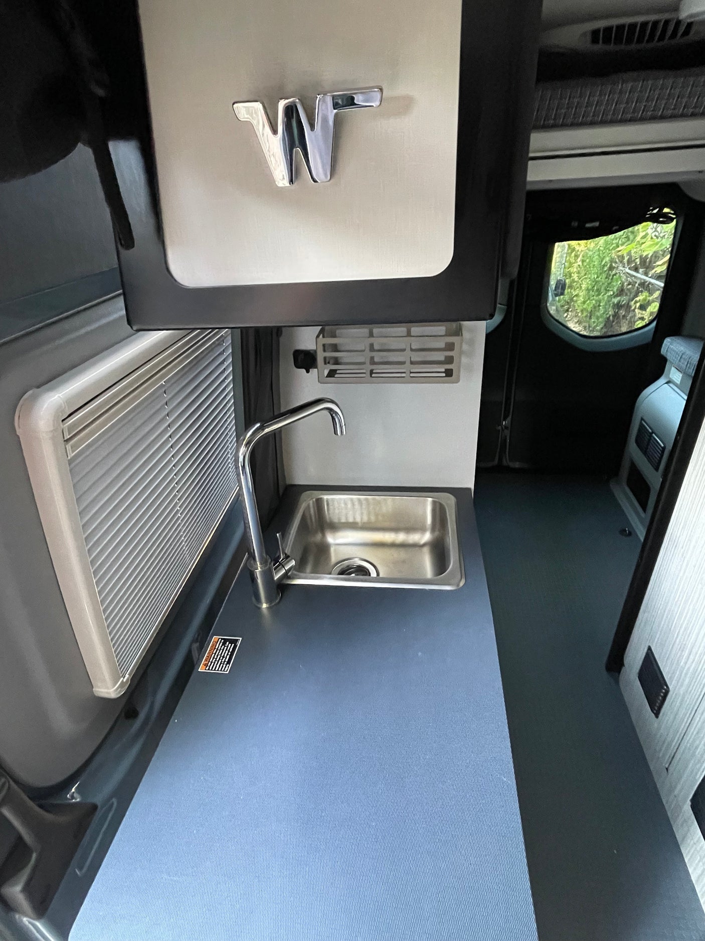 Compact Winnebago RV rental kitchen with stainless steel sink, faucet, and light blue counter.