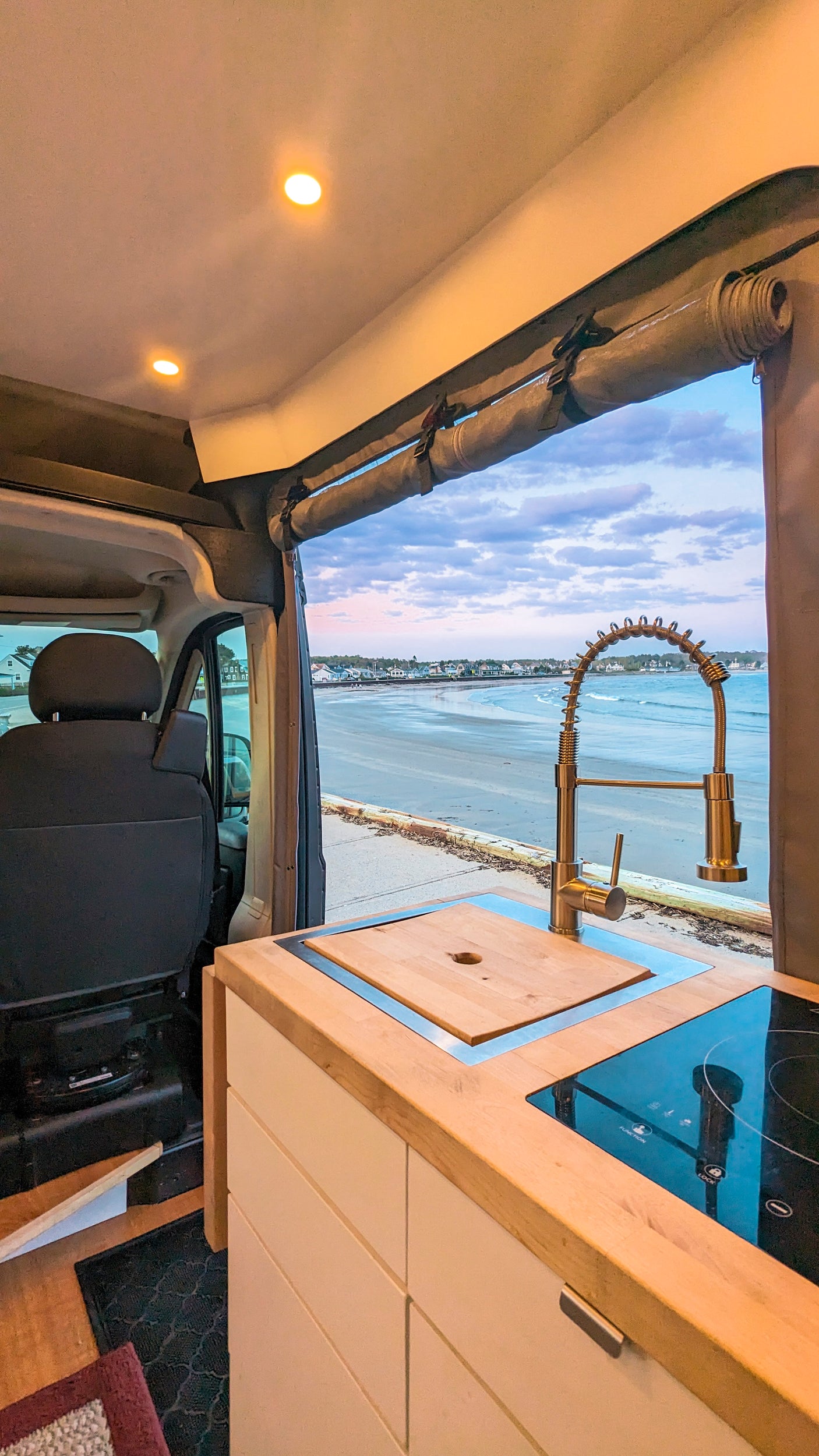Coastal escape in an **rv rental**! See the beach from this van's bright kitchen, featuring a sink, faucet, and stovetop.