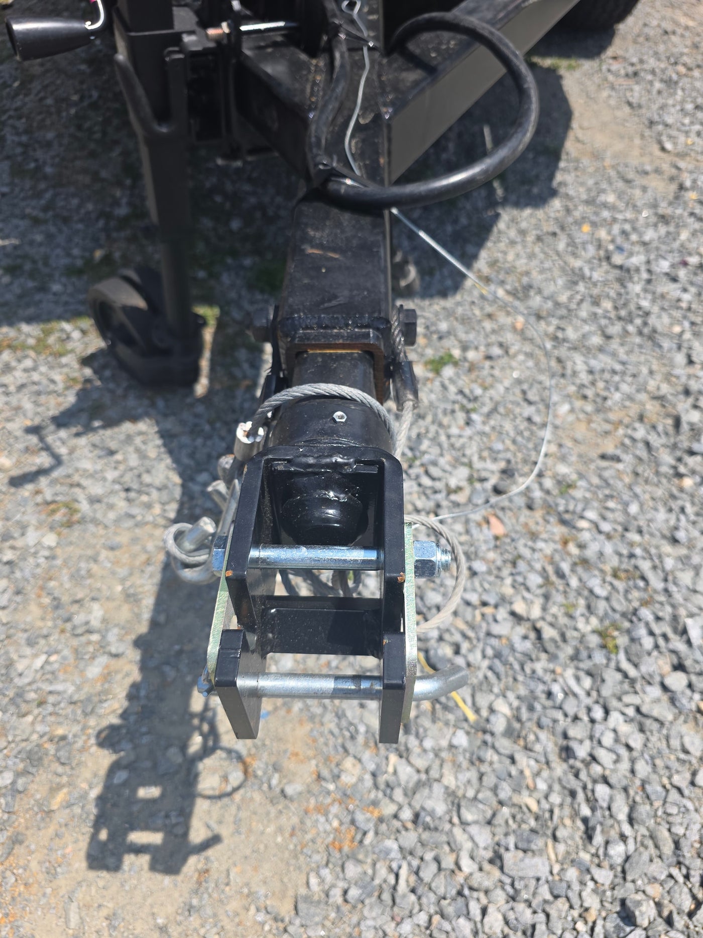 Close-up of an RV rental trailer hitch, showing the black coupler, safety cables, and attachment pins on a gravel surface. — photo 5