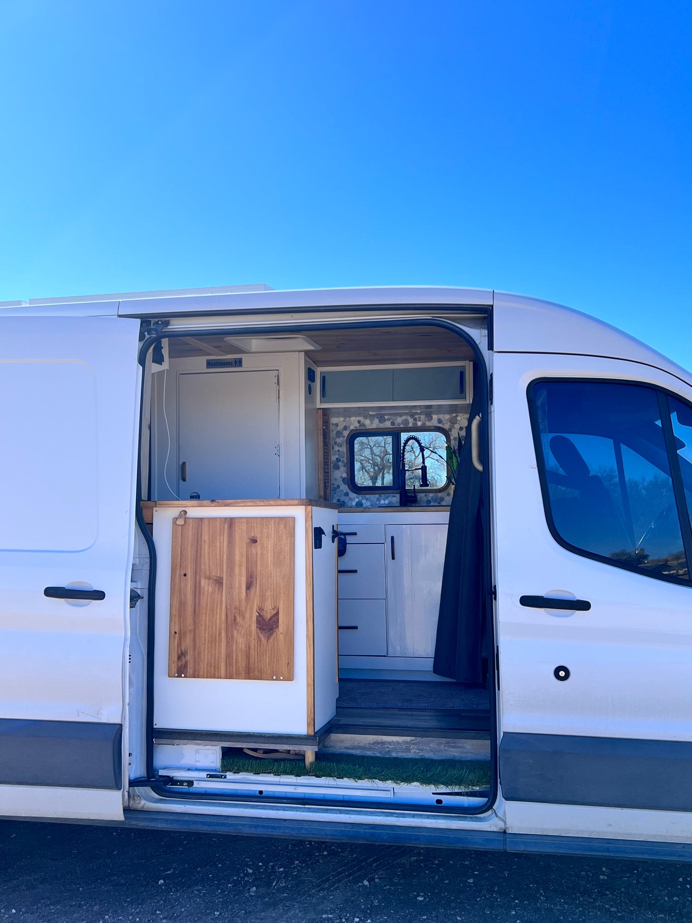 This RV rental offers a custom camper van interior with a modern kitchen, sink, and separate restroom, ready for road trips.