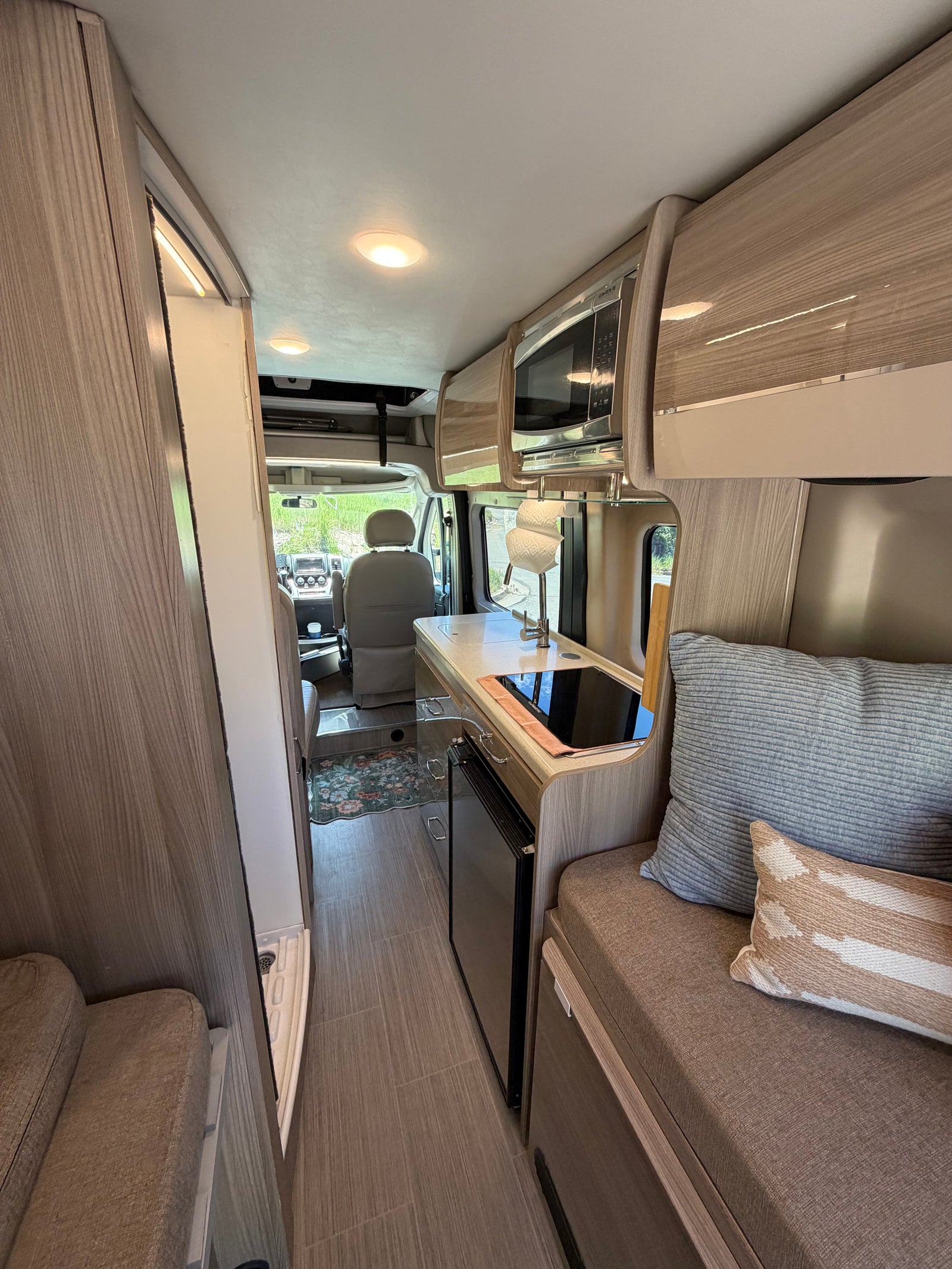 Modern RV rental interior featuring a compact kitchen with microwave, sink, and stovetop, plus comfy seating and the driver's cabin.
