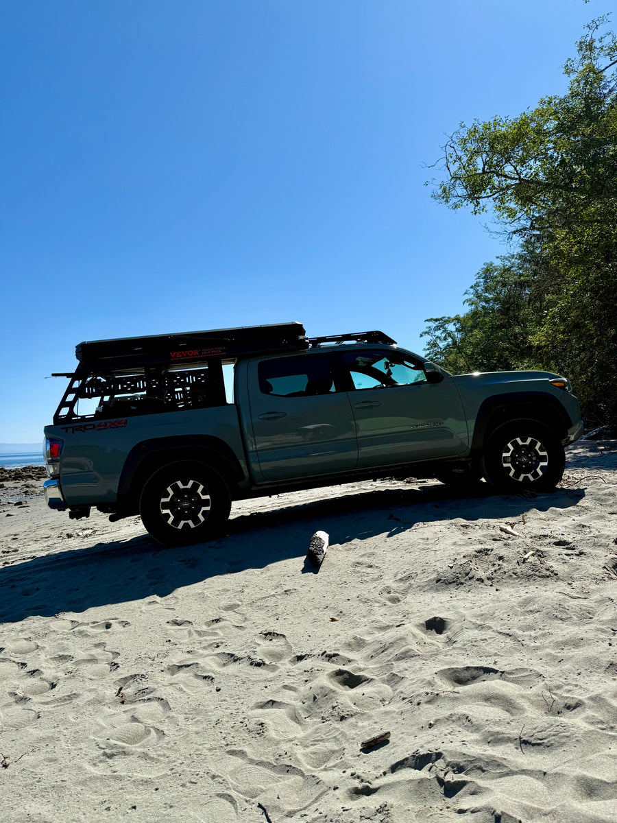 Adventure-ready grey Toyota Tacoma truck with rooftop tent parked on a sandy beach. Great for an rv rental outdoor escape!