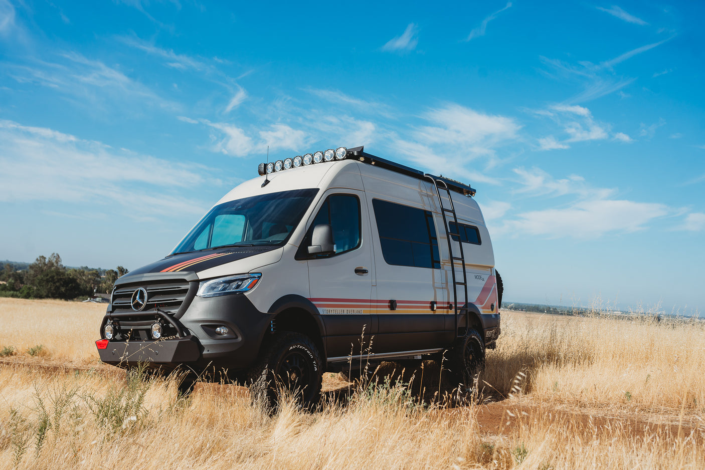 An off-road Storyteller Overland camper van, great for an RV rental adventure, parked in a golden field under a blue sky.