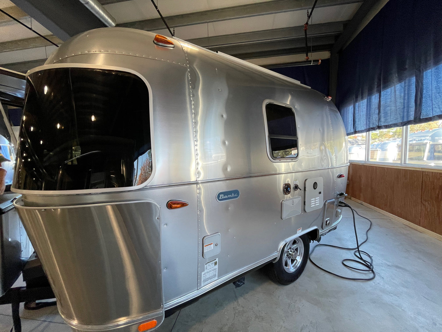A sleek Airstream Bambi travel trailer, ready for an rv rental, is parked indoors with a power cord connected.