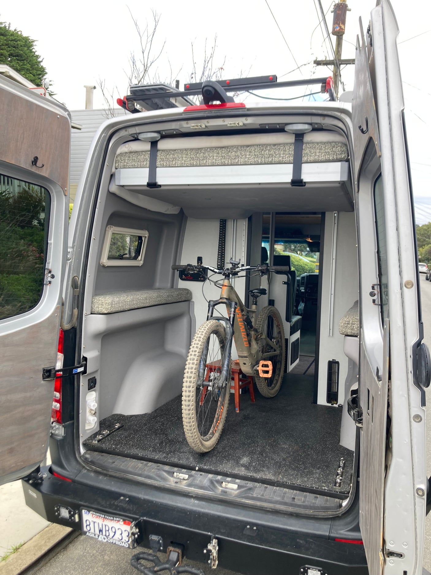 Camper van RV rental interior showing a mountain bike, elevated bed, and functional storage for adventure.