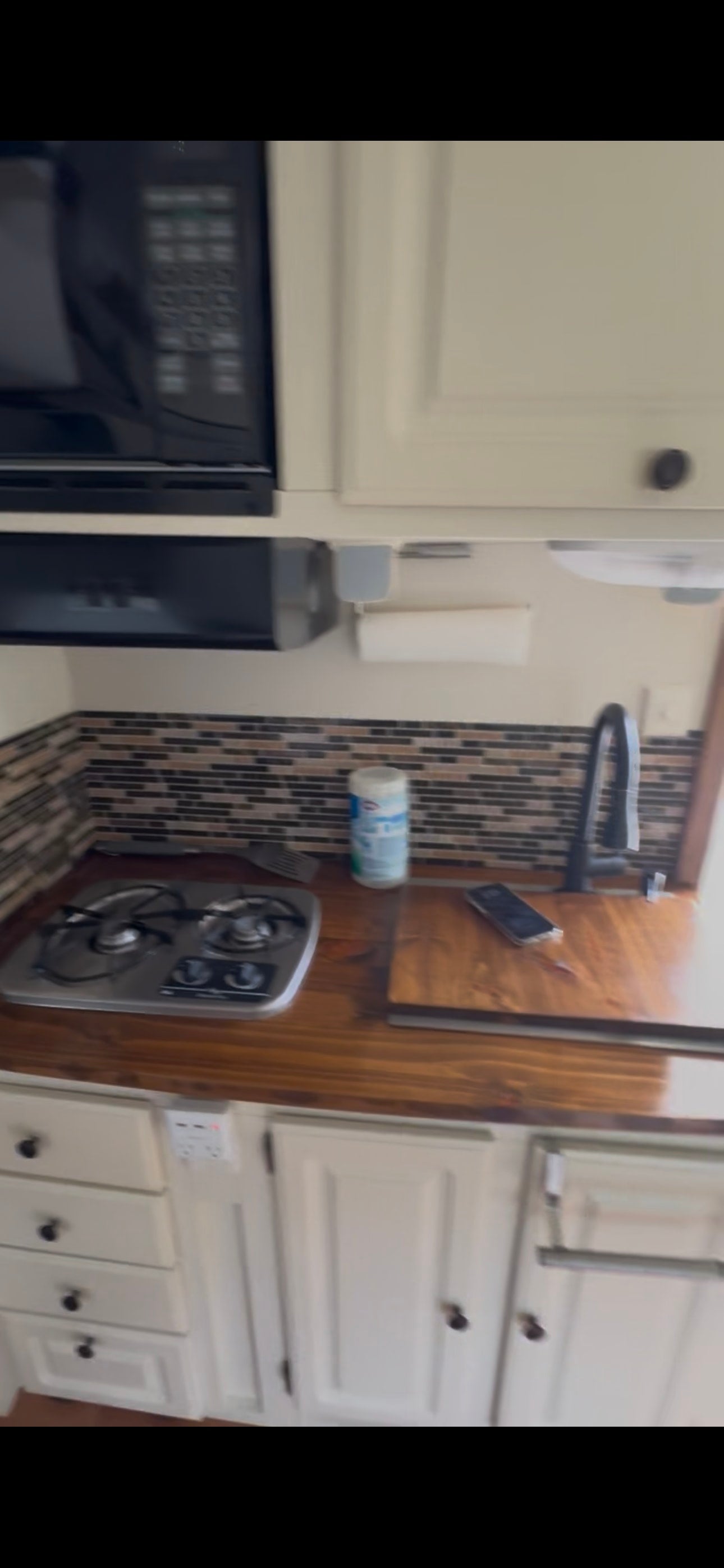 RV rental kitchen featuring a compact stovetop, sink, microwave, and ample storage for convenient mobile cooking.