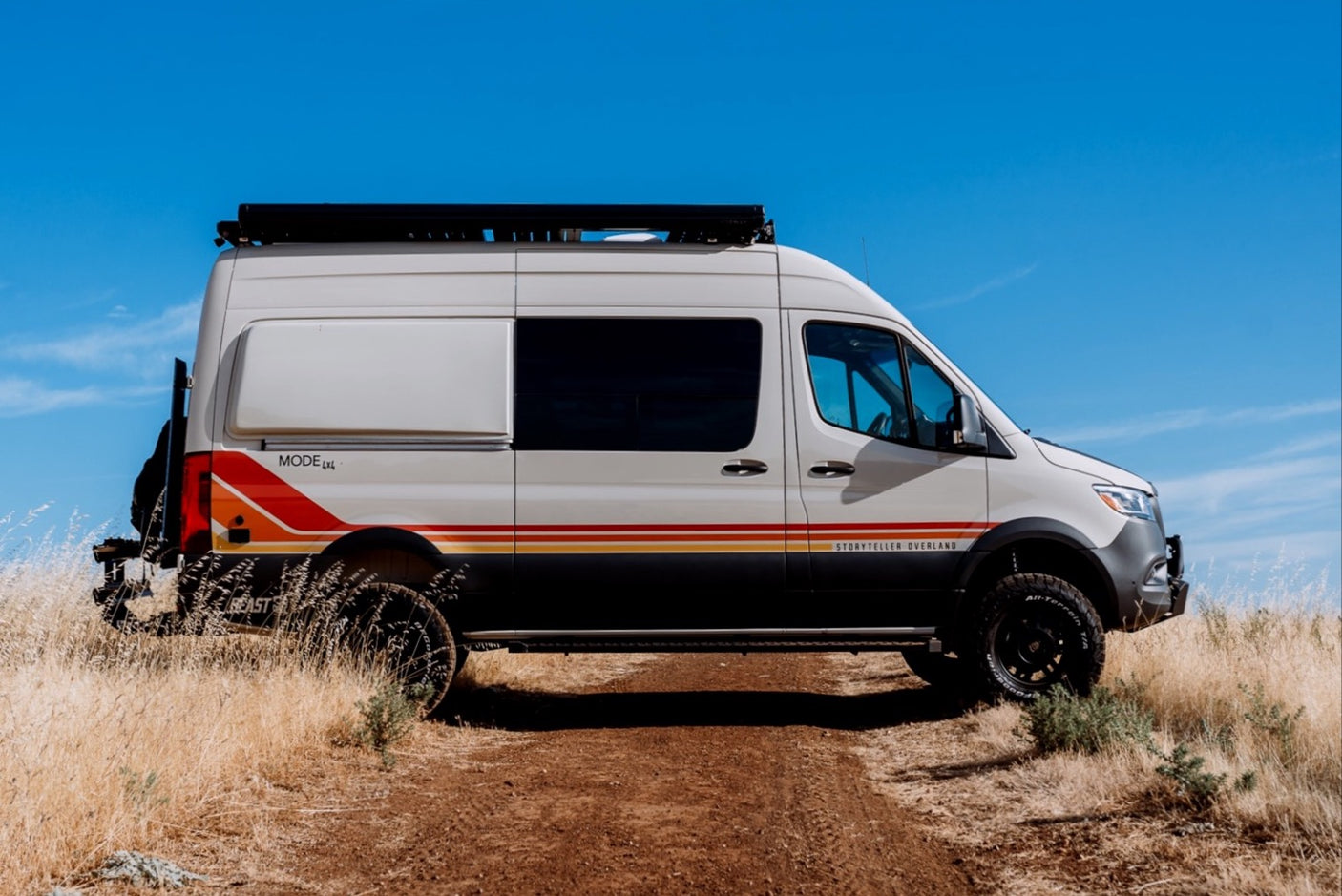 Storyteller Overland MODE 4x4 camper van, perfect for rv rental adventures, on a dirt path under a clear blue sky.