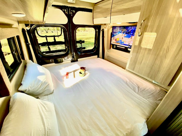 is parked on a sunny sandy beach by the blue ocean.|Experience coastal freedom! Dark grey RV rental with awning & pop-top set up on a sandy beach under a clear blue sky.|||RV rental interior: comfortable dinette with laptop & mug on light-colored seating