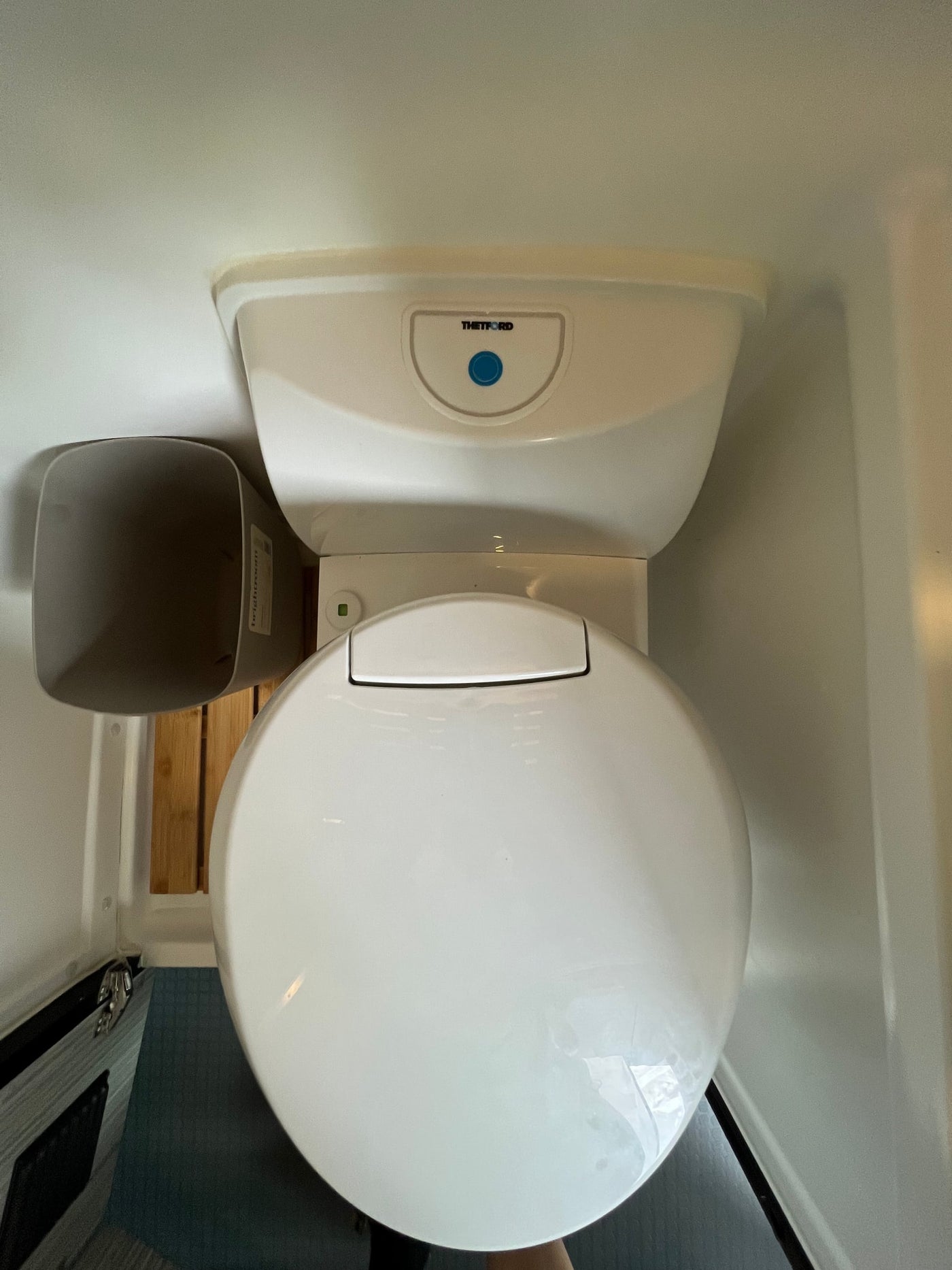 An overhead view of a clean, white Thetford toilet in a compact RV rental bathroom, with a grey waste bin nearby. — photo 14
