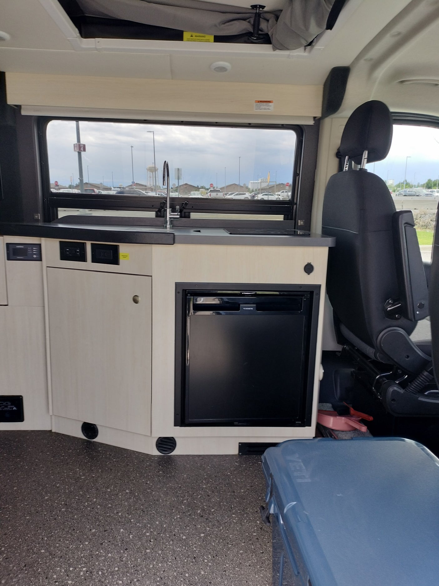Rv rental interior: Compact kitchenette with sink, Dometic fridge, induction cooktop, control panel, and passenger seating.