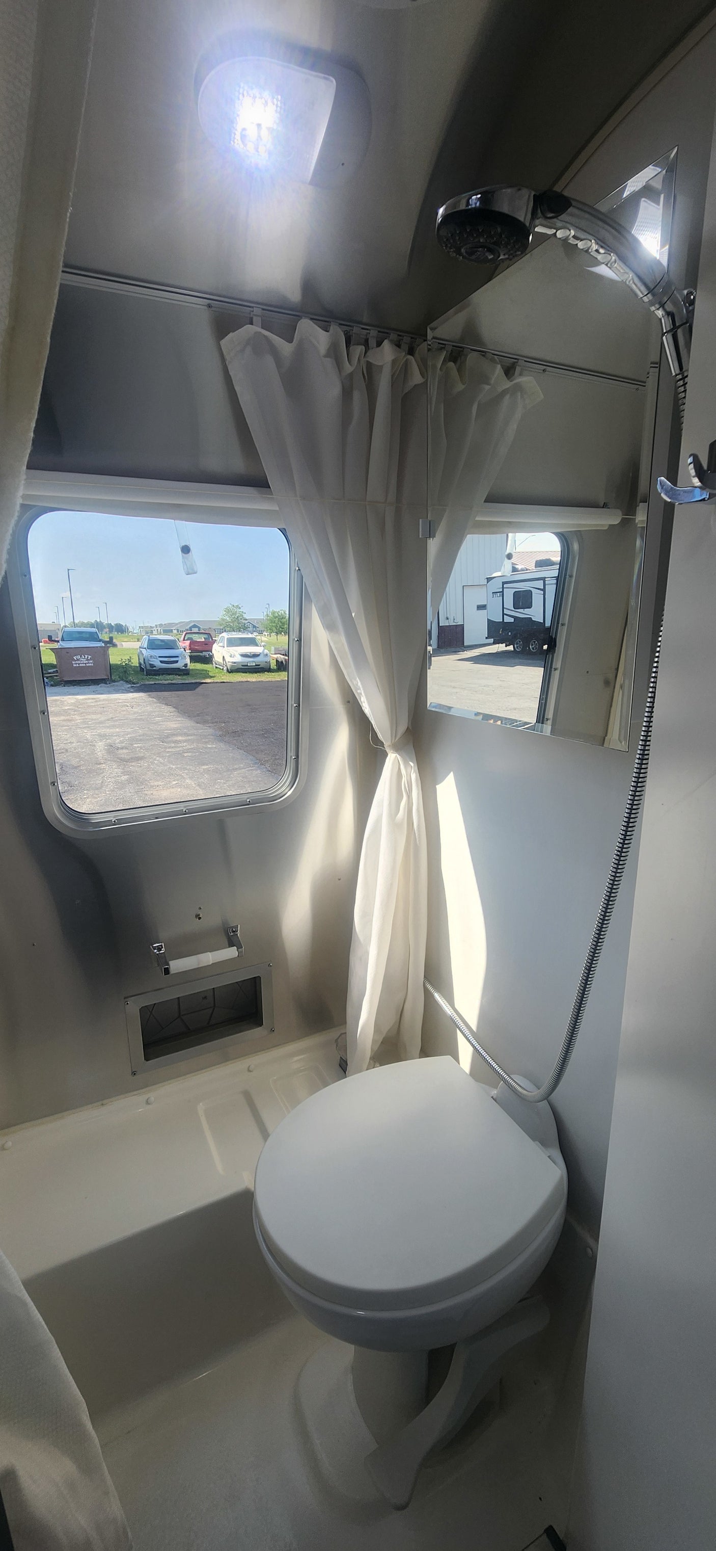 Interior of an RV rental bathroom with a toilet, shower, windows, and bright ceiling light, showing compact design.