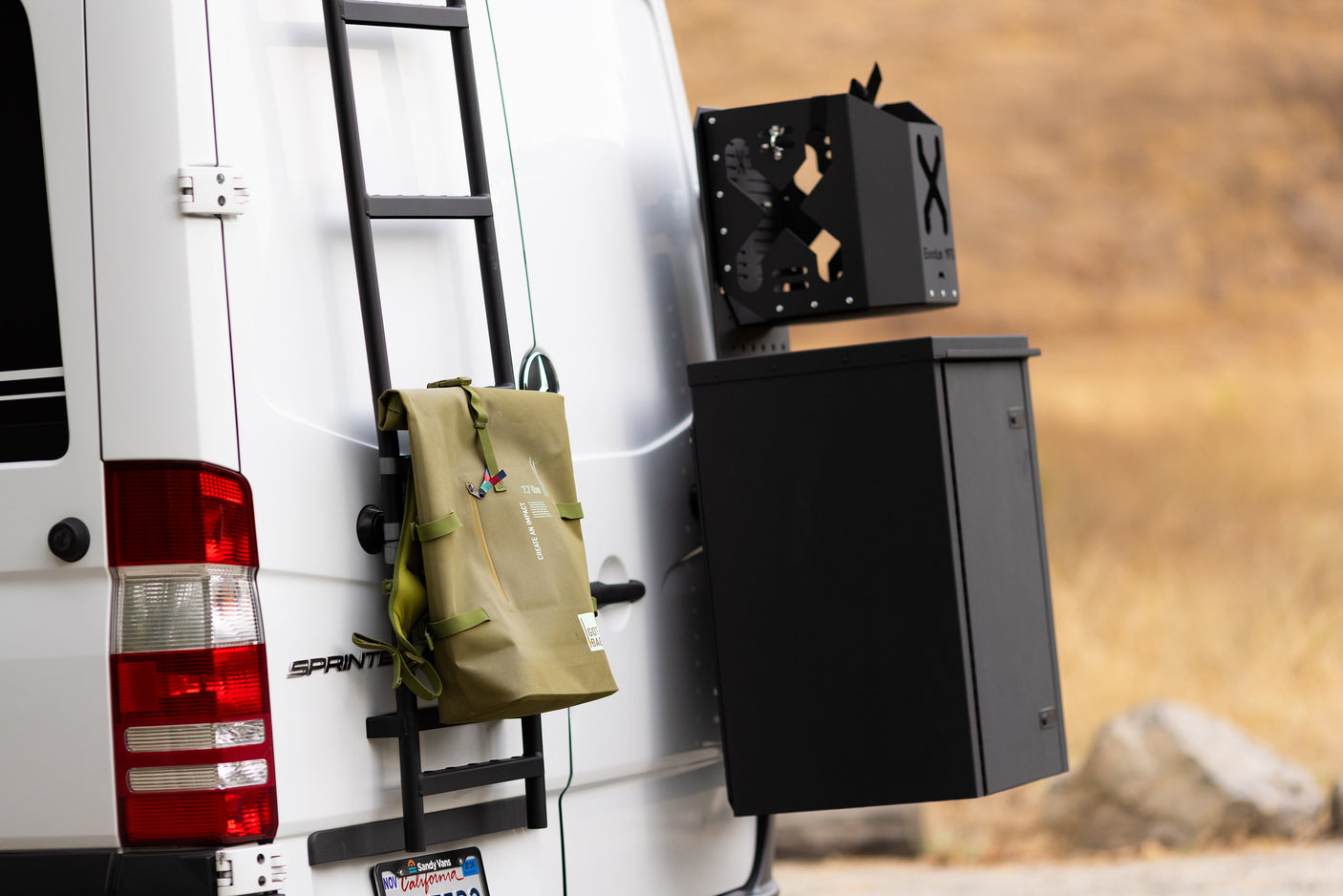 Rear of a white Sprinter RV rental van, featuring an adventure ladder, backpack, and ExoTek storage.