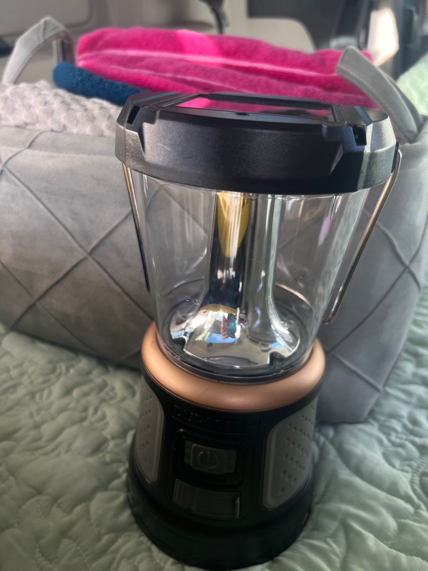 Duracell portable lantern, ready for an RV rental trip, sits on a quilted bedspread with a storage basket & towels.