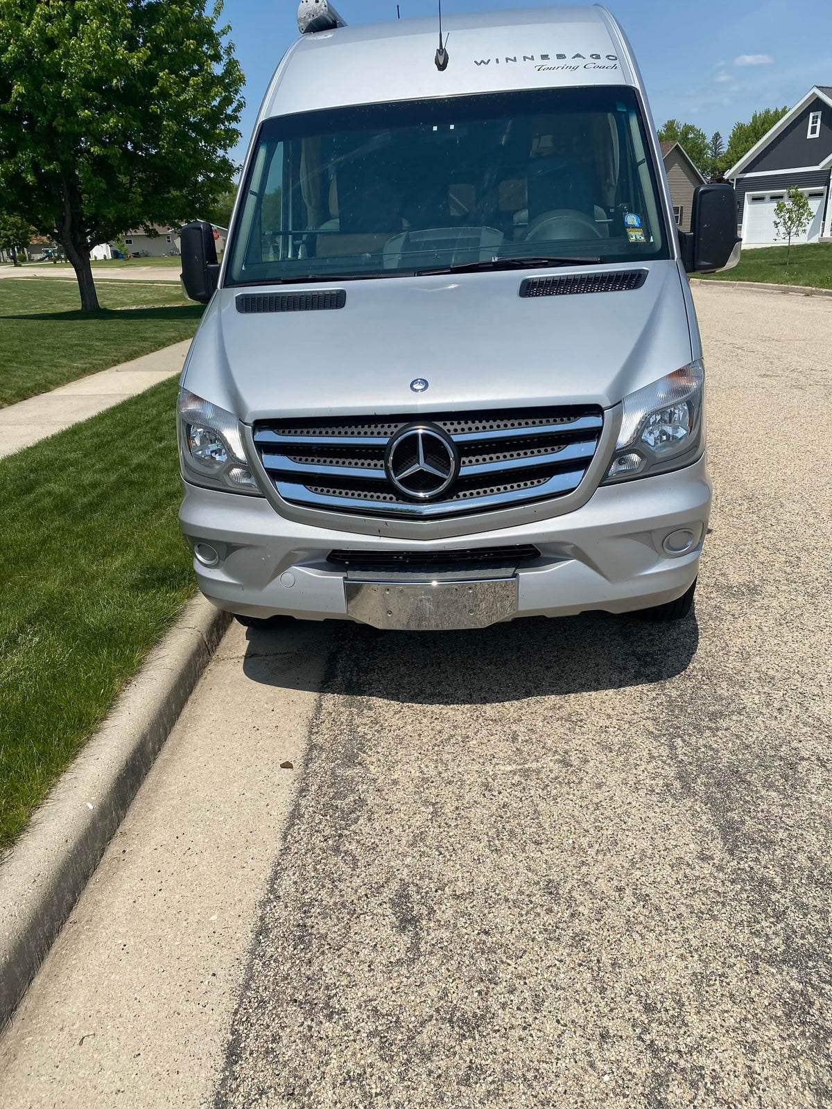 This silver Winnebago Touring Coach rv rental is parked on a sunny suburban street, ready for your next road trip adventure. — photo 3
