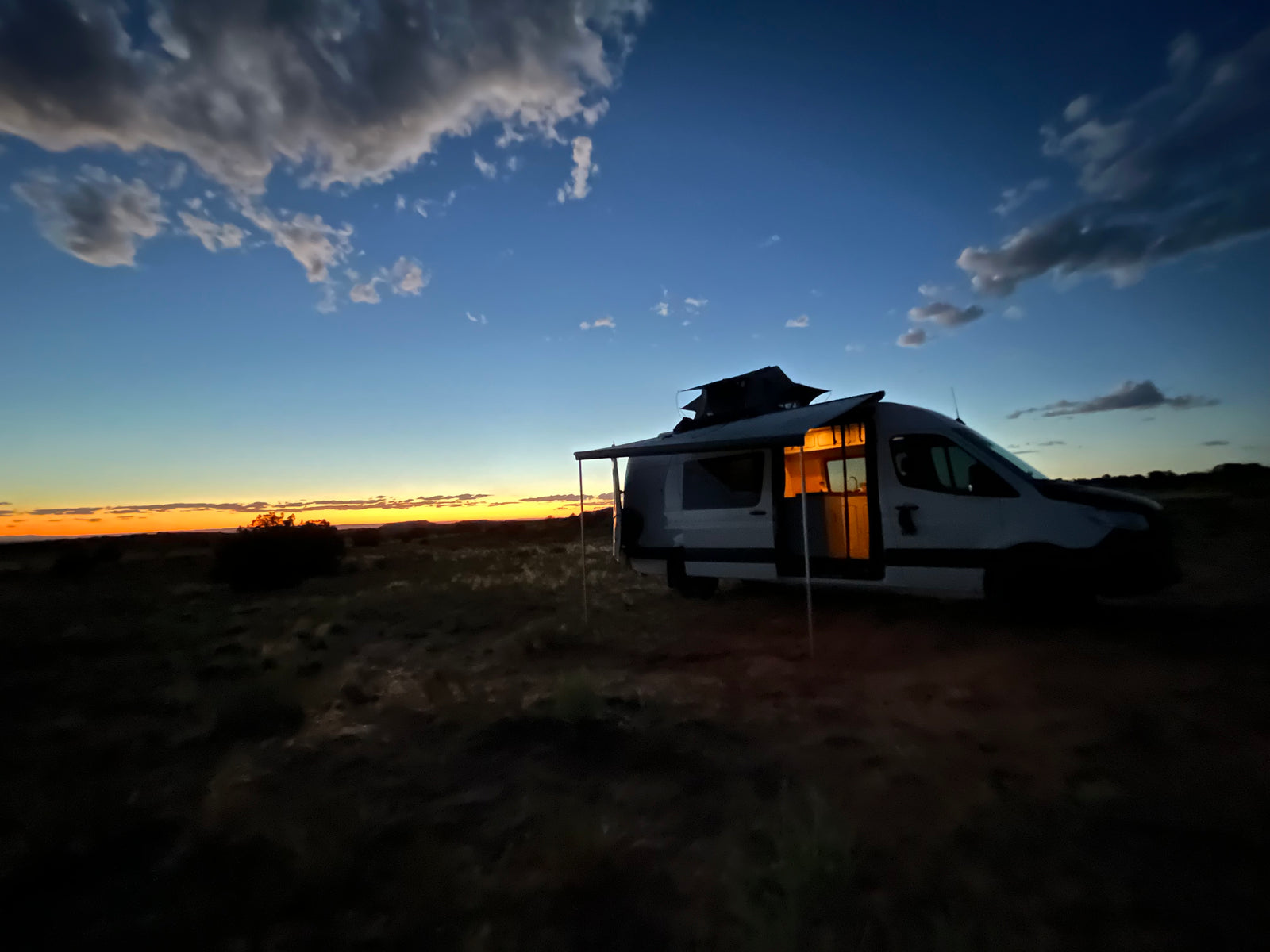 An RV rental parked at sunset in a vast desert. Interior lights glow, showcasing cozy amenities for off-grid camping.