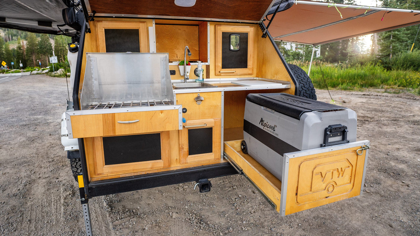 Experience convenient outdoor cooking with this RV rental's built-in kitchen: stove, sink, and pull-out Alpicool fridge for camping.