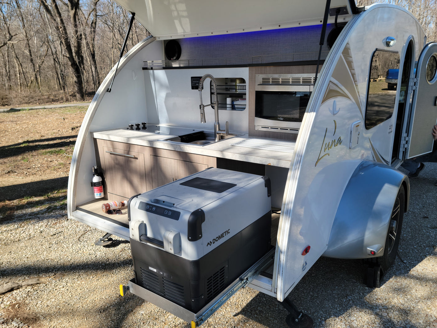 Teardrop RV rental's open rear reveals a modern outdoor kitchen with sink, stove, microwave, and Dometic cooler.