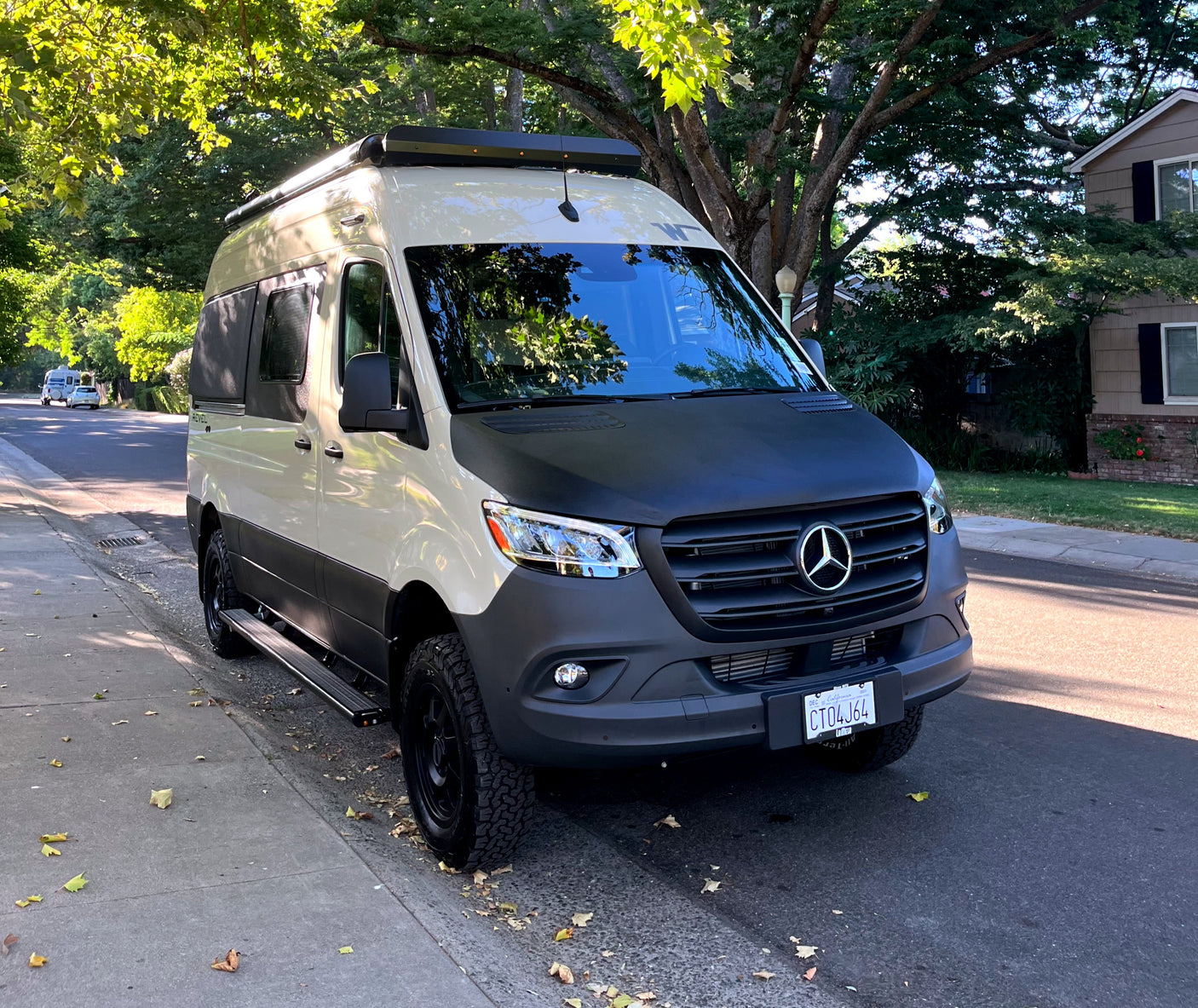 Custom two-tone Mercedes Sprinter camper van, perfect for RV rental adventures, parked under trees on a sunny street.
