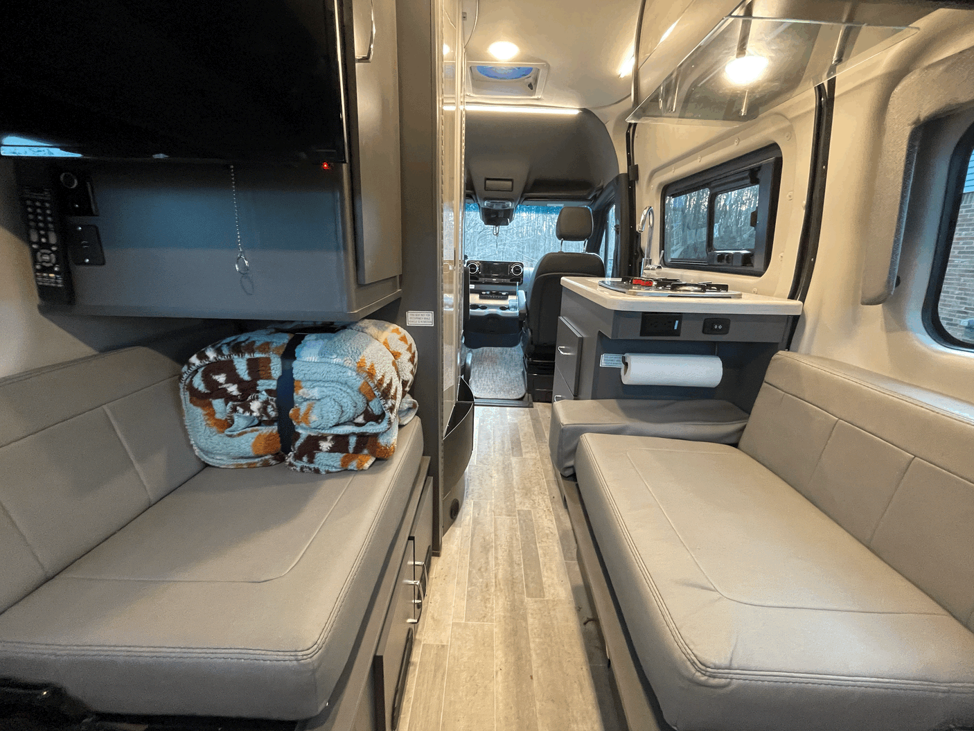 Inside this RV rental, a view down the aisle reveals a compact kitchen, comfy seating, and a TV for mobile travel.