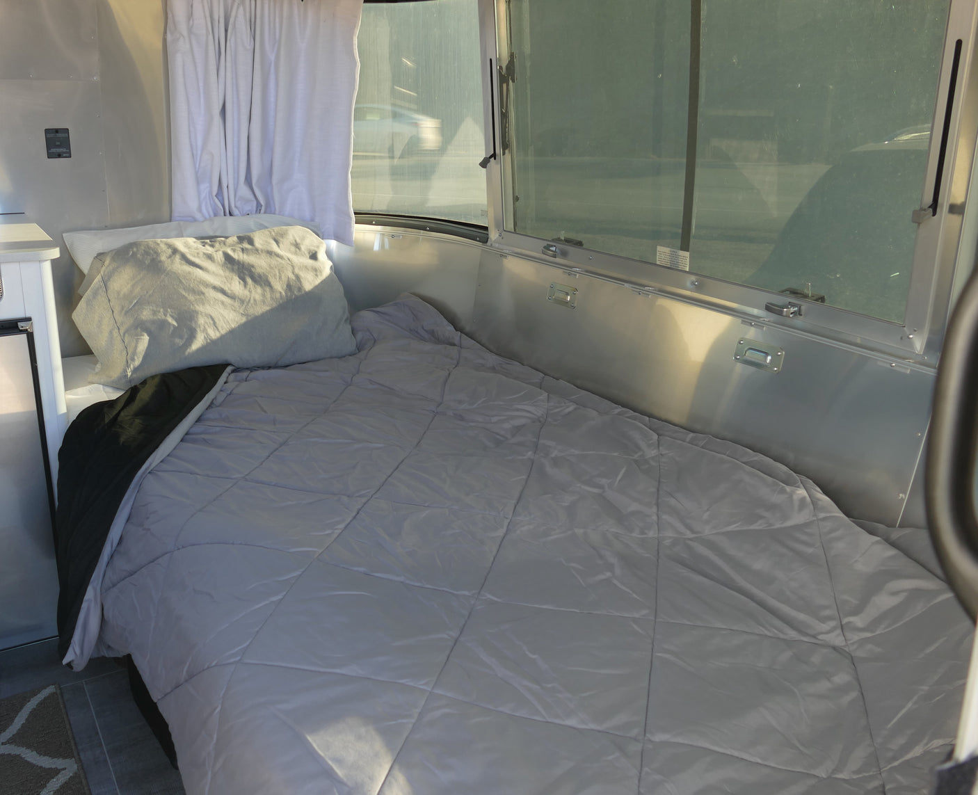 Bright RV rental interior: a comfy bed by panoramic windows, offering a glimpse of the passing road.