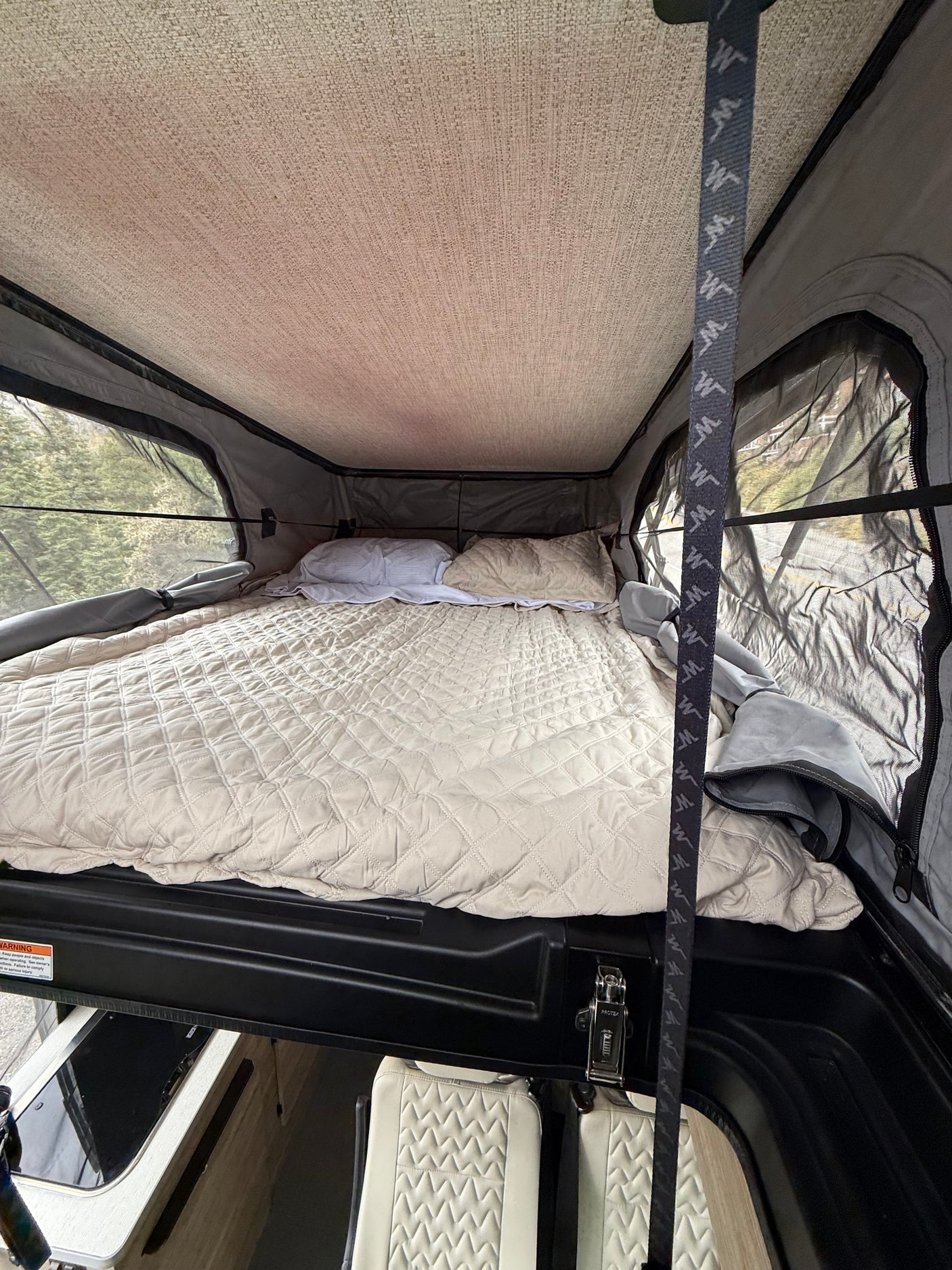 Cozy rv rental pop-top camper bed with quilted comforter & mesh windows offering outdoor views for a comfortable night.