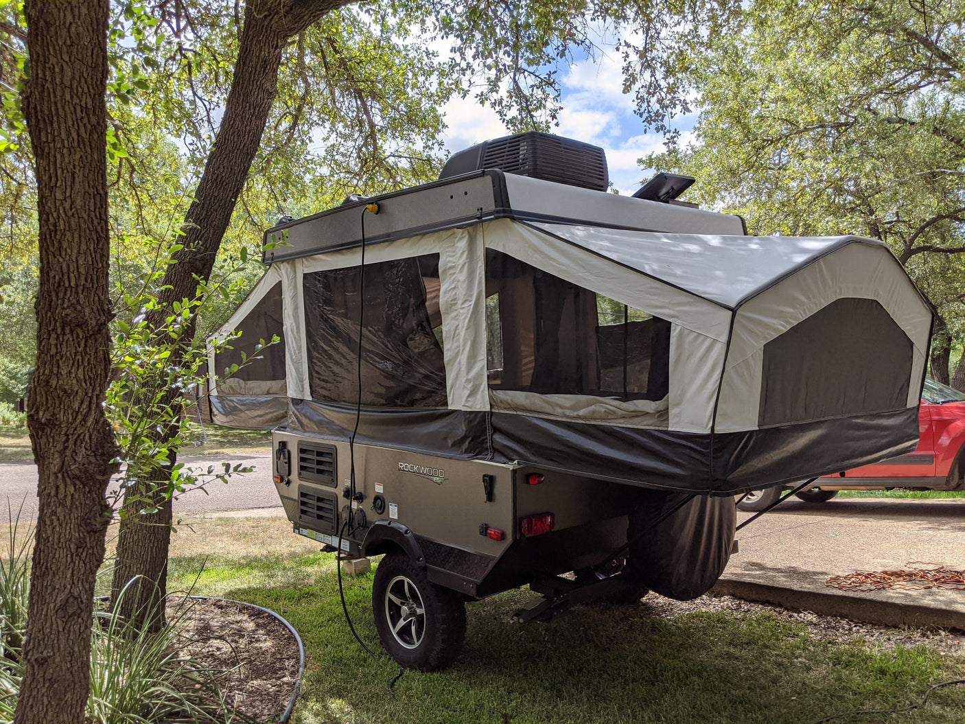 A Rockwood ESP pop-up camper at a shady campsite, fully extended. Perfect for an RV rental adventure.