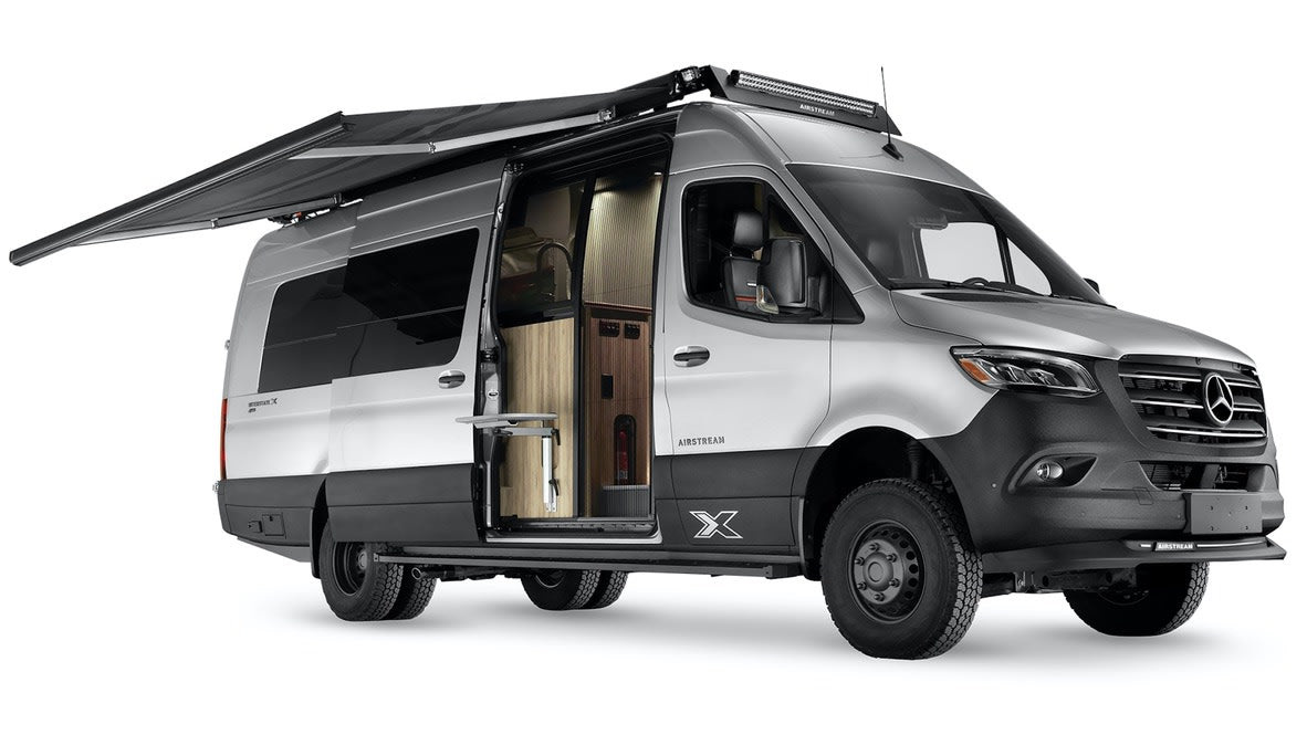 Rugged silver Airstream camper van with extended awning & open door, revealing interior. Ideal for your next rv rental adventure.